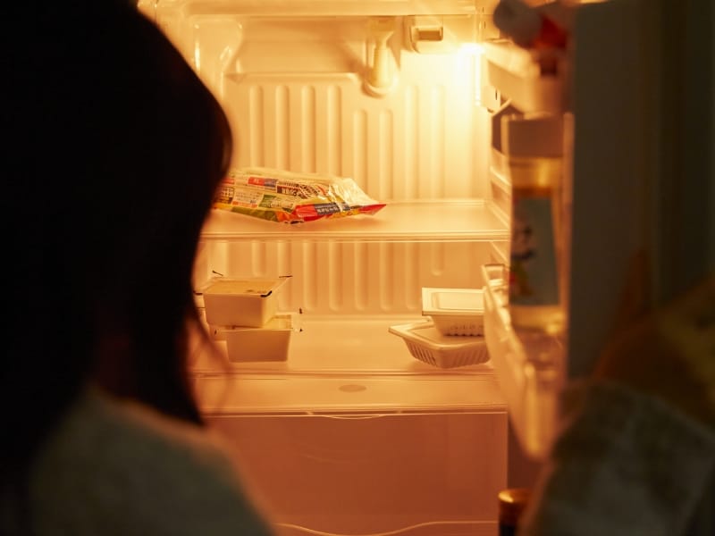 ほとんど食べ物の入っていない冷蔵庫をのぞく子どもの後ろ姿
