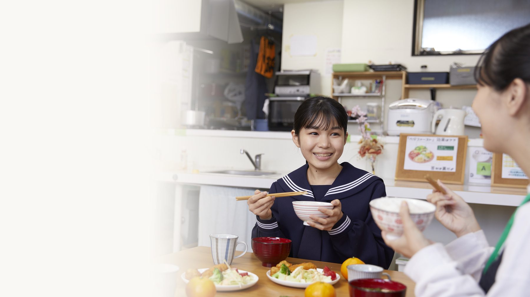 放課後教室で、スタッフと一緒に笑顔でご飯を食べる制服姿の生徒