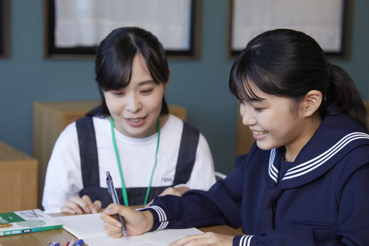 スタッフに教わりながら、笑顔でノートに書き込む制服姿の生徒