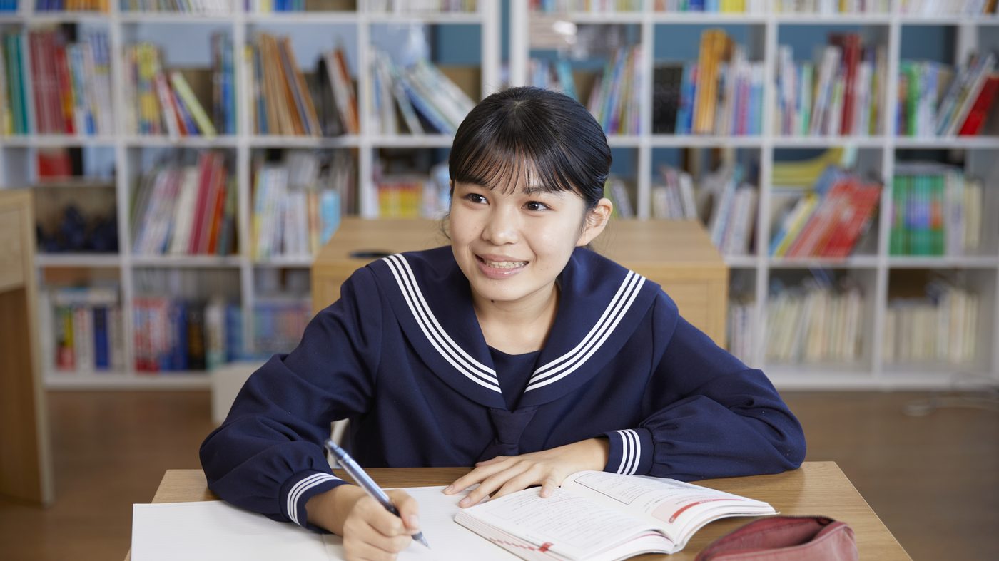 参考書とノートを広げ、ペンを持って笑顔で顔を上げる制服姿の生徒